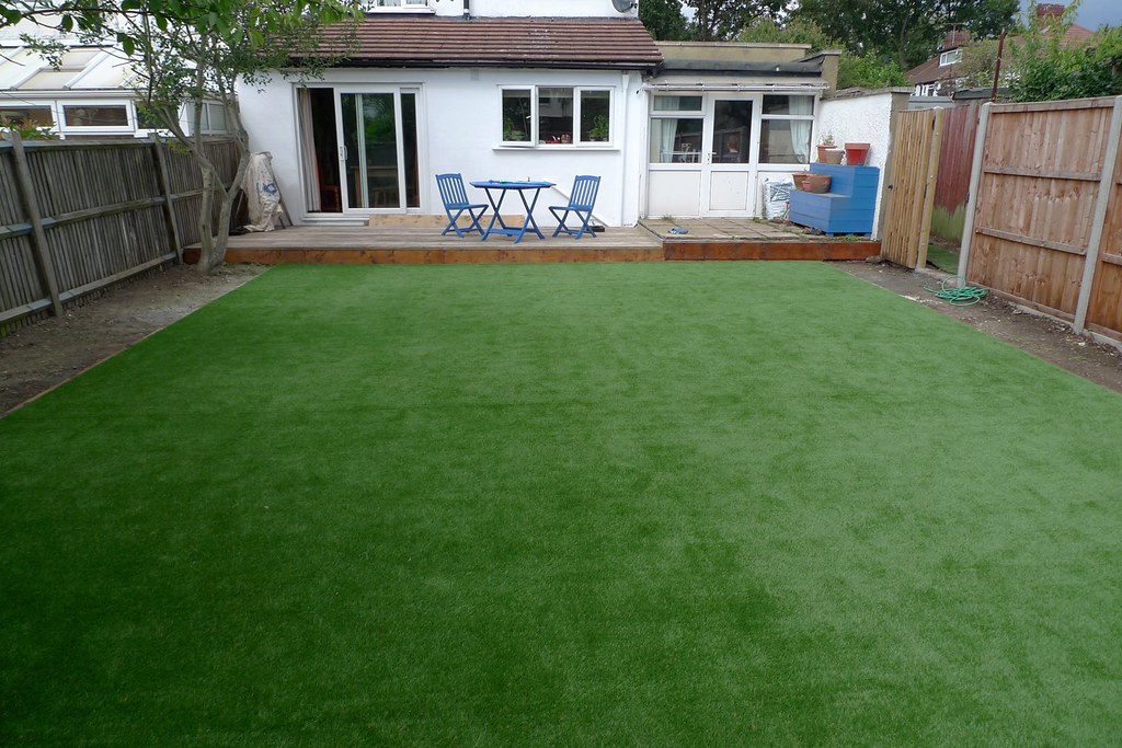 Residential backyard transformed with professionally installed artificial turf, patio deck and seating area behind a home