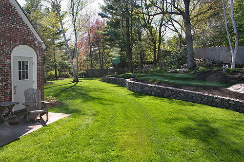 Beautiful backyard putting green with stone terracing, Adirondack chairs and flagged cup