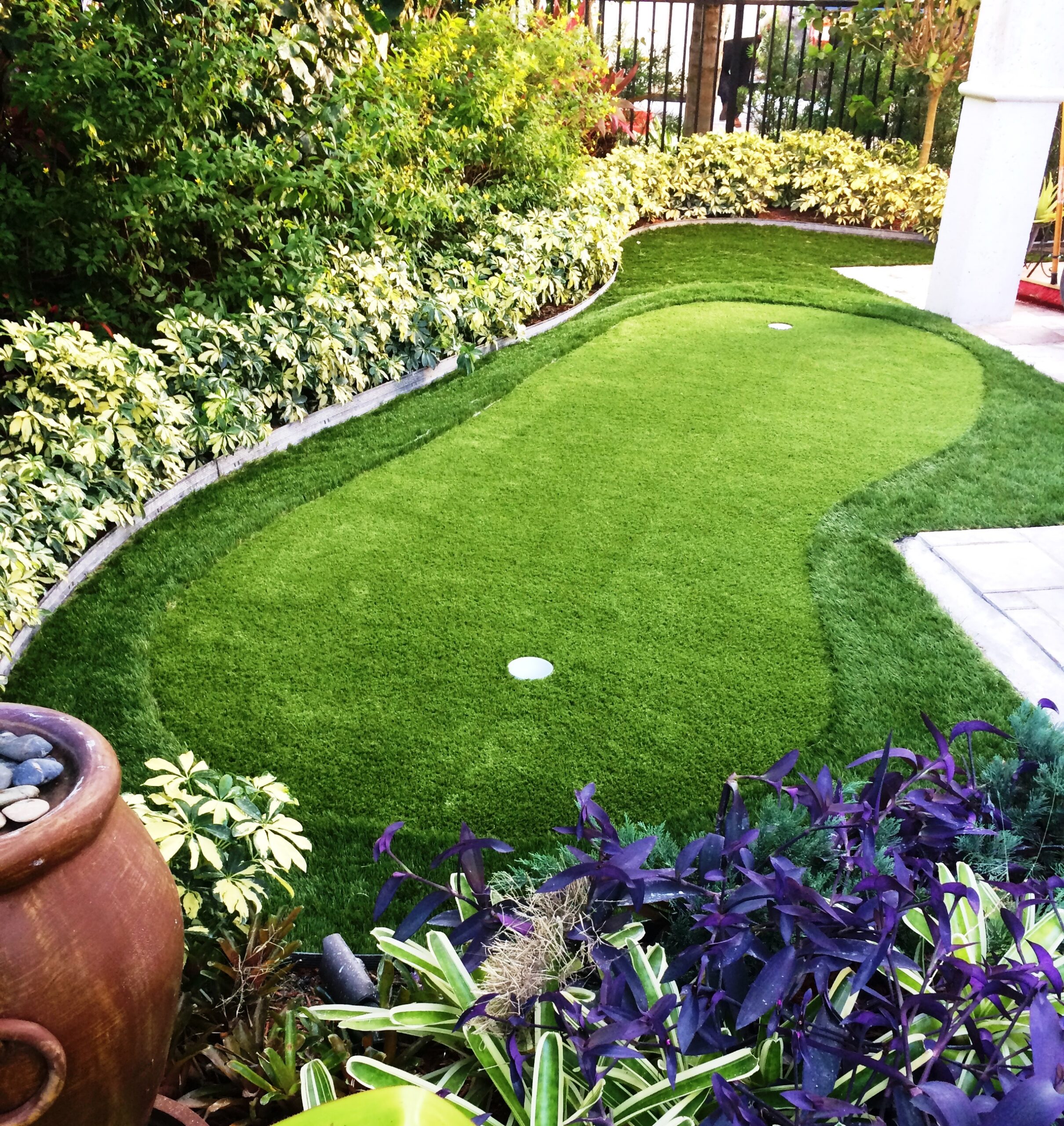 Gorgeous tropical backyard with oval artificial putting green, two holes and lush garden landscaping